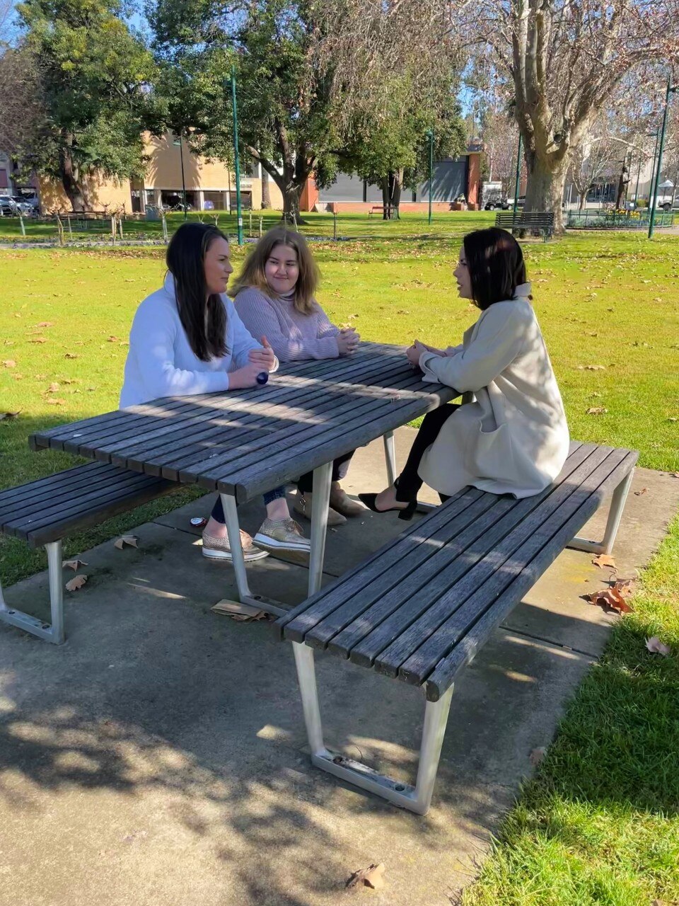 three women sitting at a bench in a park