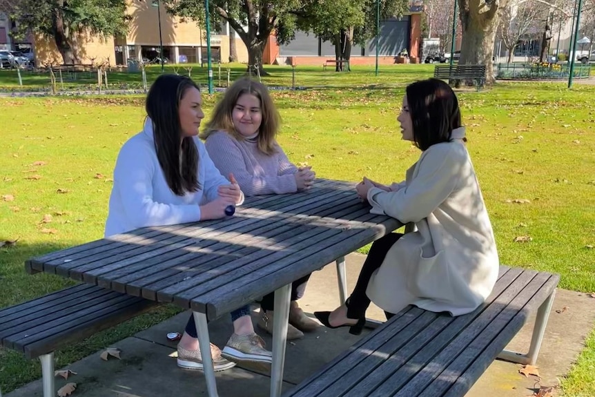 three women sitting at a bench in a park