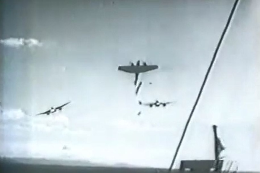 A black-and-white still image, taken from a newsreel, showing three aircraft flying above a ship.