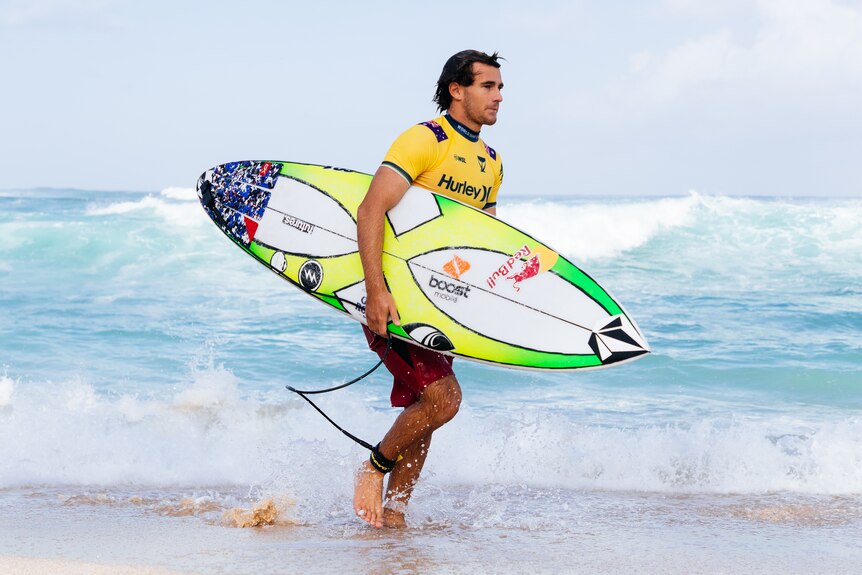 Jack Robinson walking with his surfboard under his arm after competing