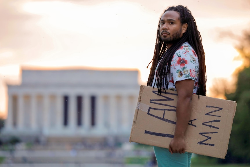 A young Black man with long braids holds a sign reading 'I am a man' near the Lincoln Memorial