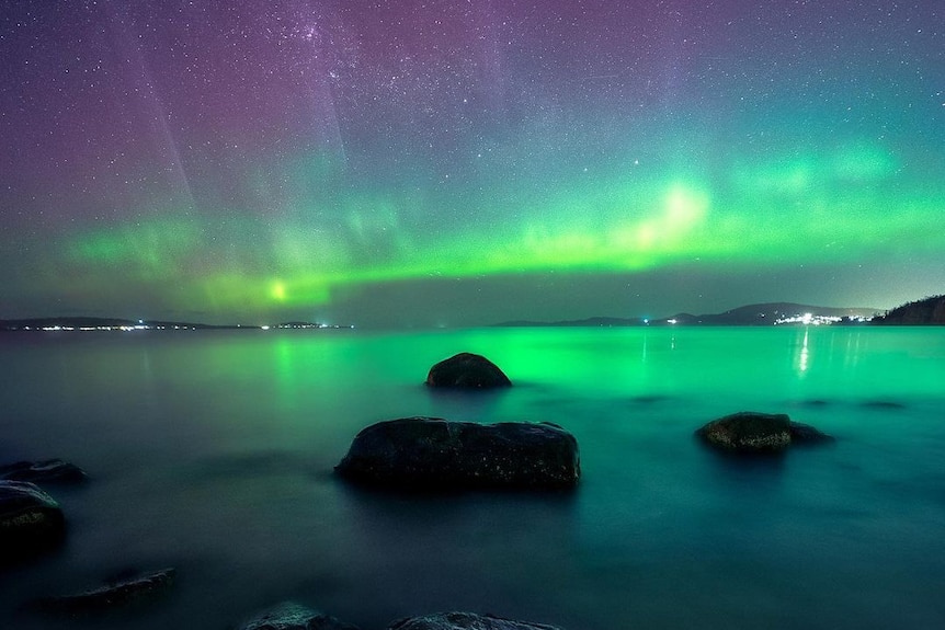 Green and purple lights in the sky seen over waterfront.