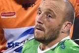 Josh Hodgson sits on the ground with people around him holding and looking at his knee