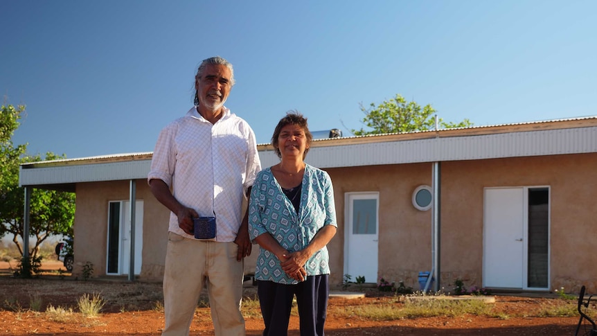 Two people stand in front of clay rendered house