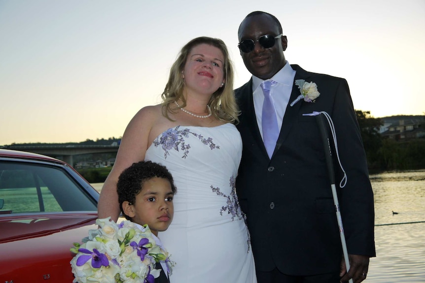 Krystal wears a white wedding dress with purple flowers. Nemoy wears a tuxedo with a purple tie. Jaden stands next to his mother