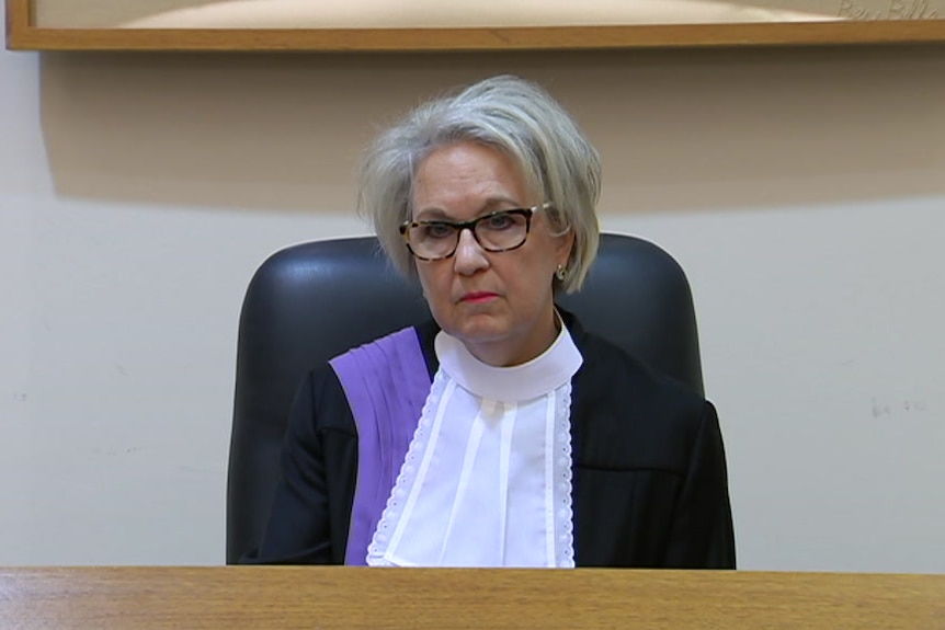 Eine Frau mit grauem Haar und Brille, gekleidet in Gerichtsroben 