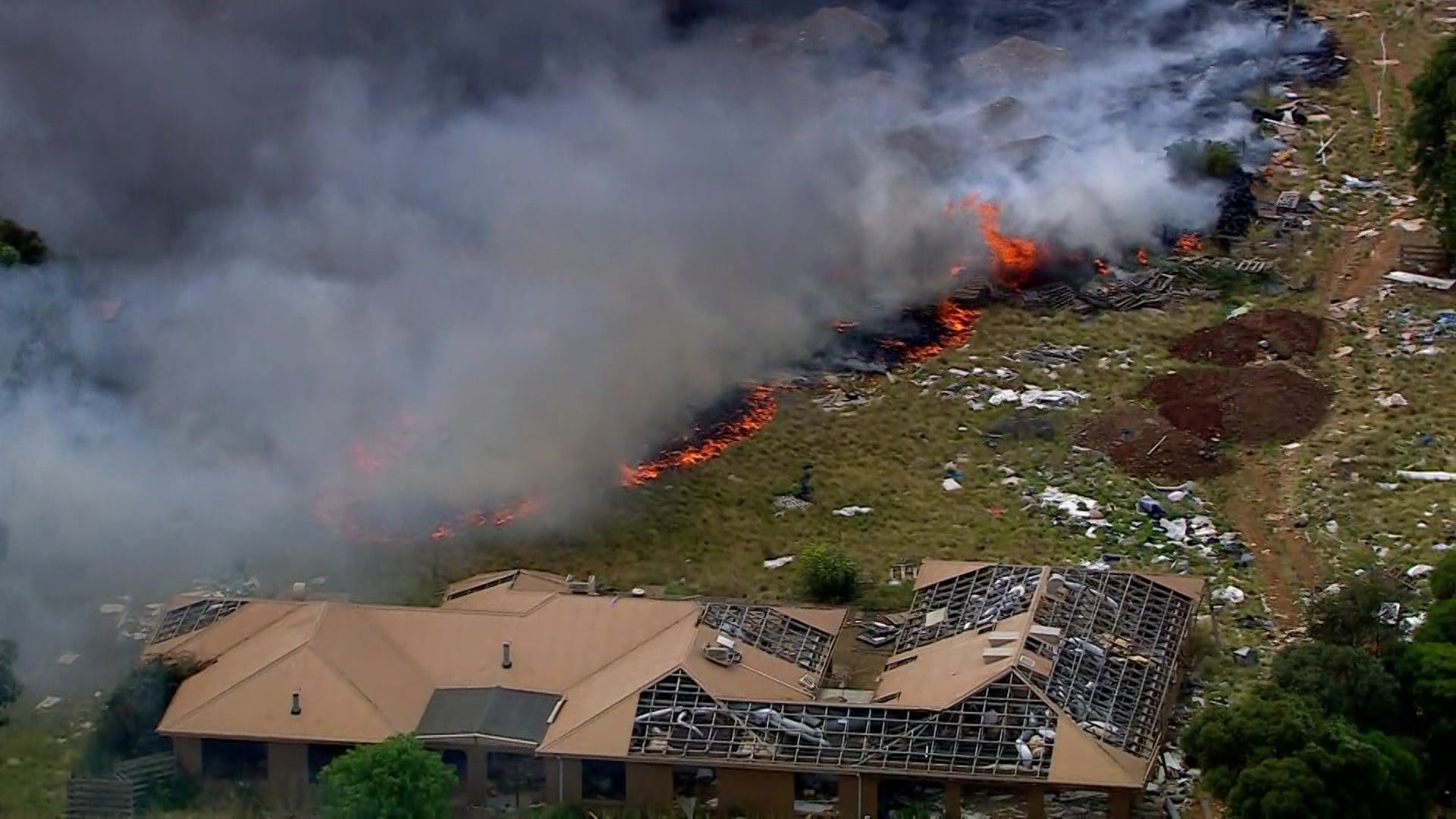 Uma foto aérea de um incêndio queimando em direção a uma propriedade decrépita com partes do telhado faltando.