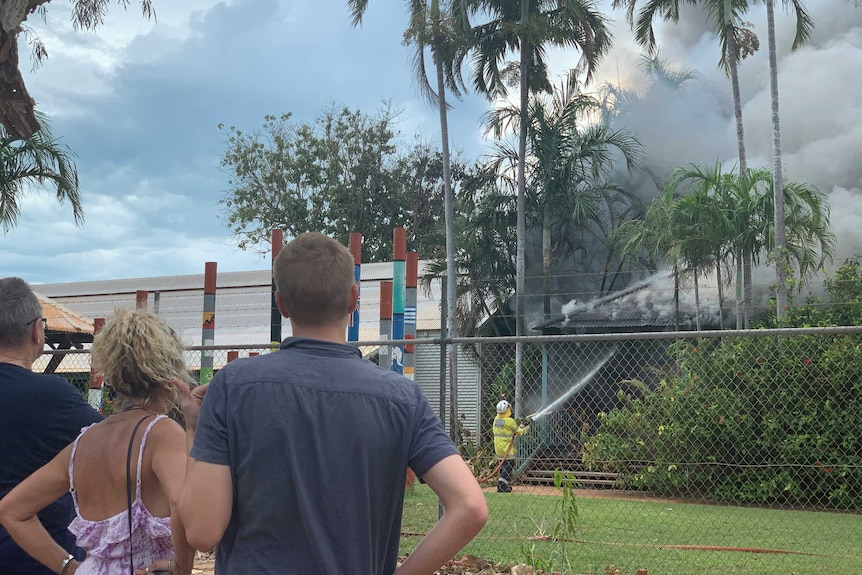 A small group of people watch a firefighter hosing down a blaze in a primary school.