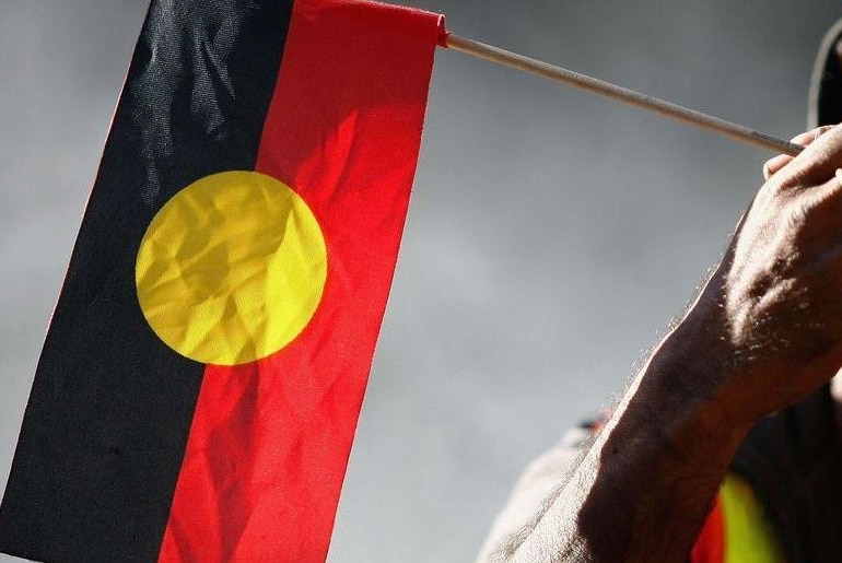 Indigenous Australian holding an Aboriginal flag