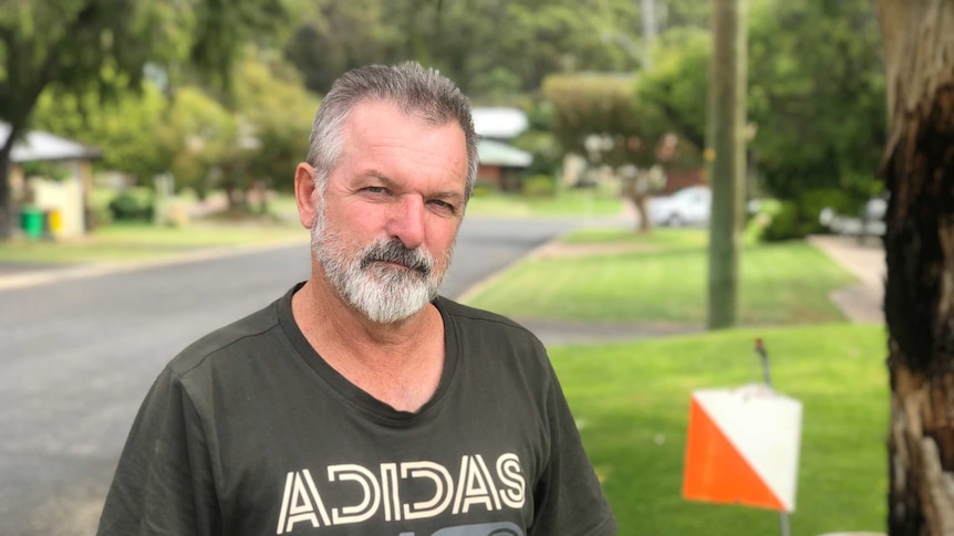 Man standing on roadside grass in front of orange and white box.