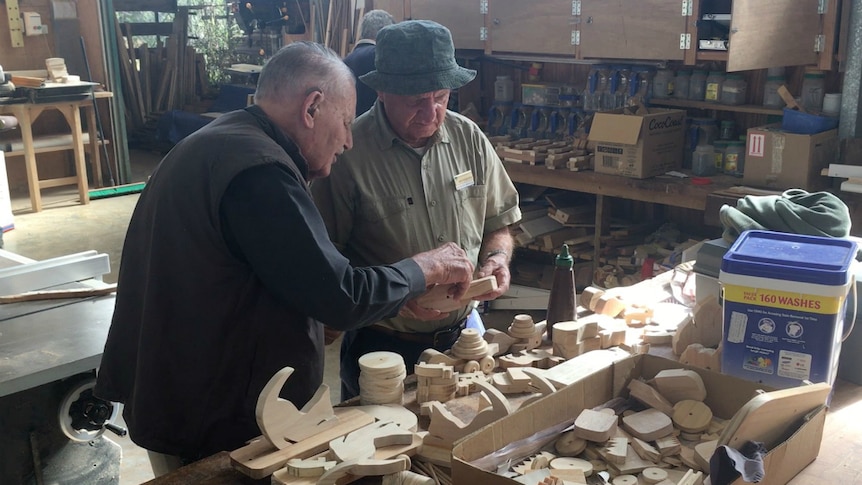 Two men looking over a small wooden toy.