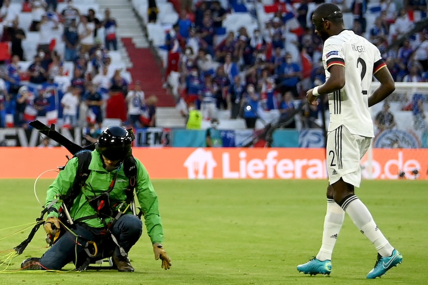 Antonio Ruediger walks towards a man in a green jumpsuit with a parachute on his back