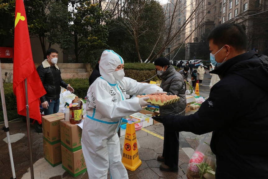 Someone wearing full PPE hands a man a tray of eggs.