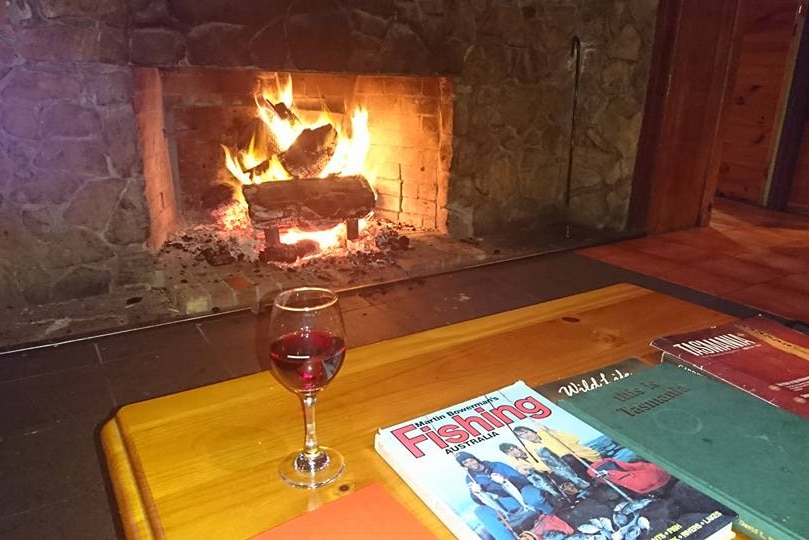 A glass of red wine on a table in front of an open fire at Bronte Park Lodge and Chalet.