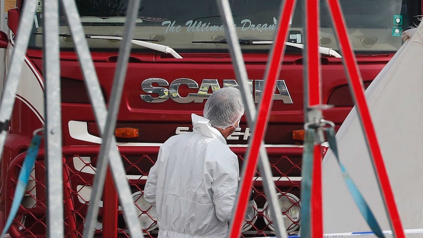 A man in a forensic suit and hairnet inspects the front of the red truck