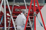 A man in a forensic suit and hairnet inspects the front of the red truck