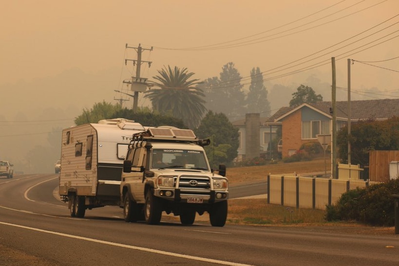 A four-wheel drive towing a caravan set against a smoky background