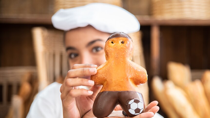 Woman holds up a donut in the shape of a football player.