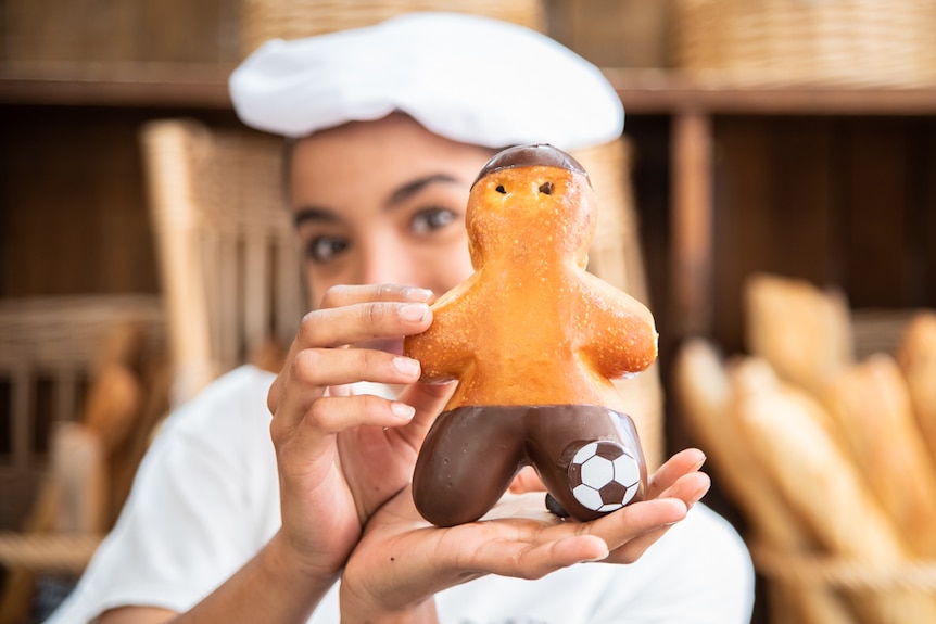 Woman holds up a donut in the shape of a football player.