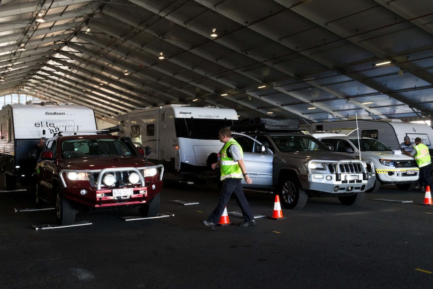 Four-wheel-drives towing caravans being weighed in a large shed by compliance inspectors.