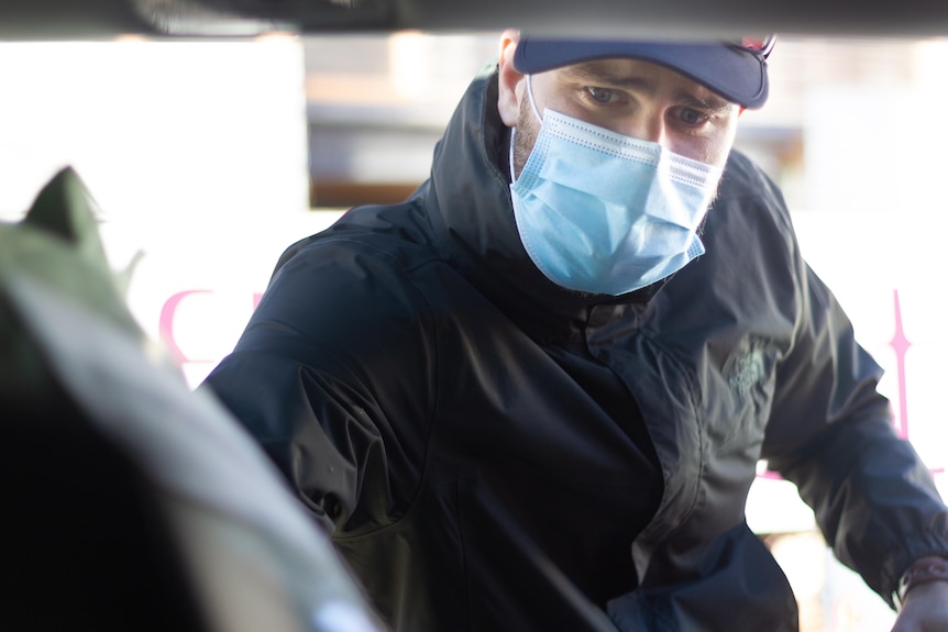 A man wearing a face mask puts a bunch of flowers into the back of his car. 