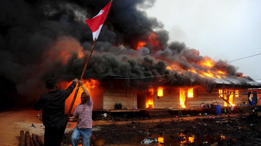 Two men remove the Indonesian flag as the compound of the Gafatar sect burns after being set on fire by local villagers
