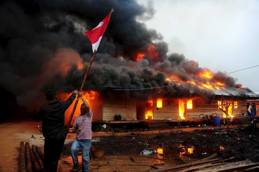 Two men remove the Indonesian flag as the compound of the Gafatar sect burns after being set on fire by local villagers