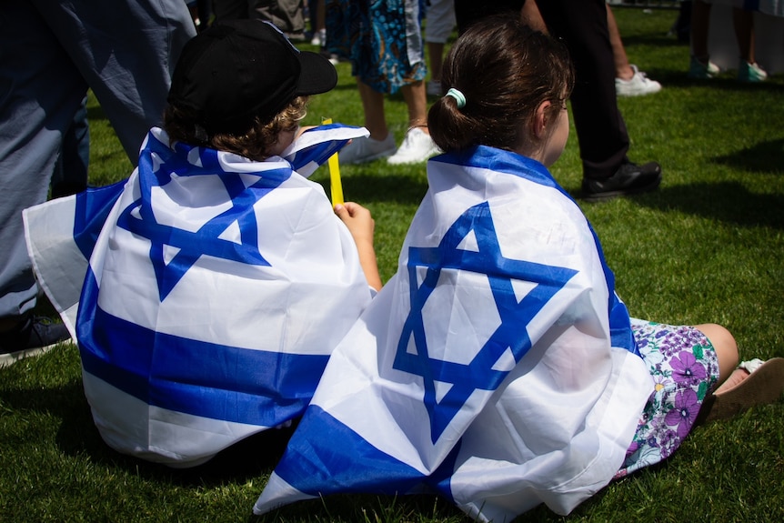 the back of two young children wearing an israeli flag at a rally at moore park in sydney