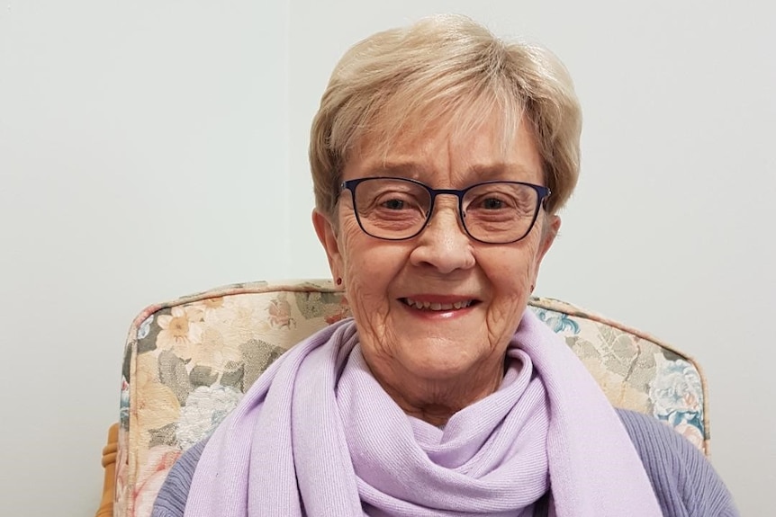 A portrait of an older, bespectacled woman wearing a pastel scarf.