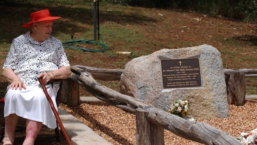 Lady Flo Bjelke-Petersen sits on a chair with her cane next to the headstone of her husband's grave