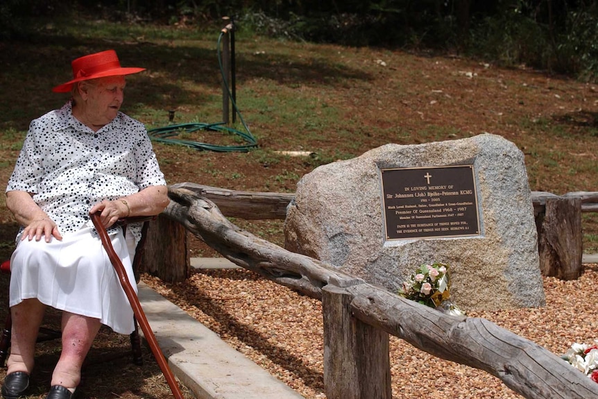 Lady Flo Bjelke-Petersen sits on a chair with her cane next to the headstone of her husband's grave