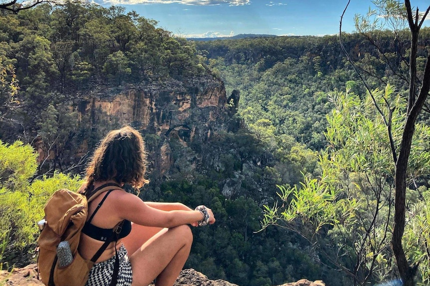 A young woman looks out over the tree tops of a national park.