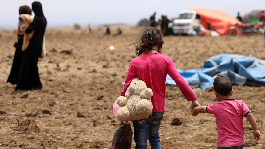 An Internally displaced girl from Deraa province carries a stuffed toy and holds the hand of a child