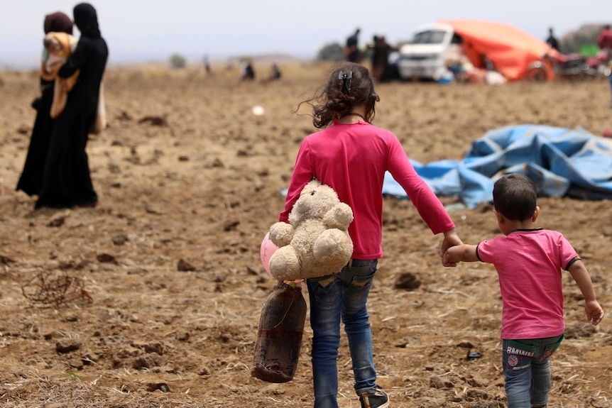 An Internally displaced girl from Deraa province carries a stuffed toy and holds the hand of a child