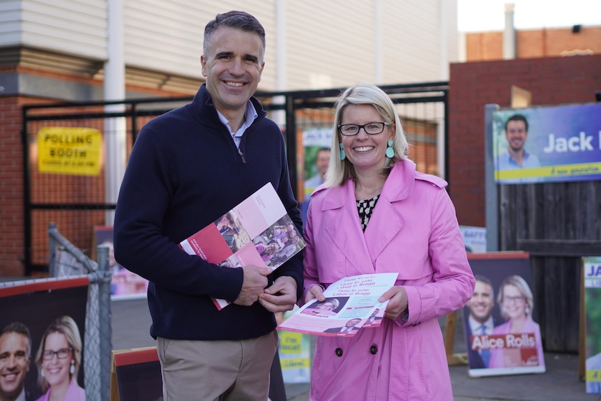 A man wearing a jumper and a woman wearing a pink jacket holding how to vote cards