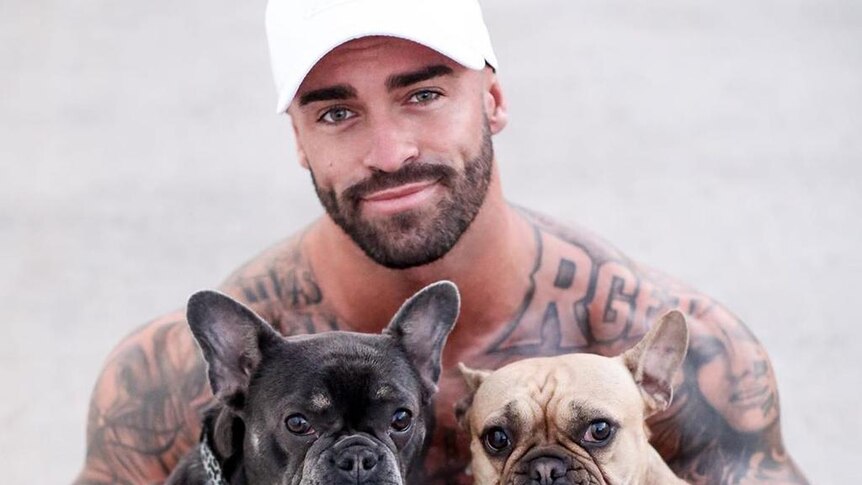 A shirtless man carrying two dogs