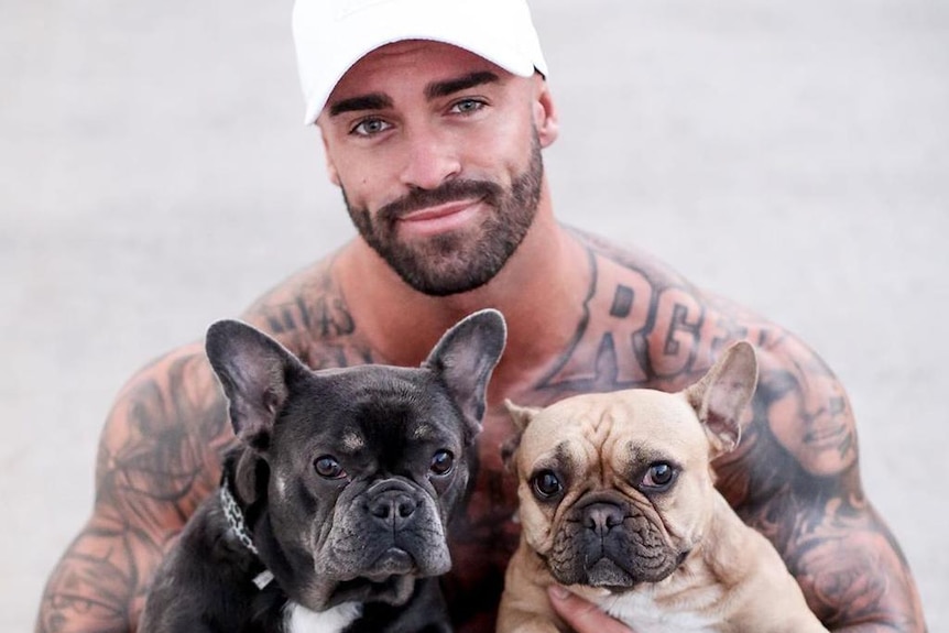 A shirtless man carrying two dogs