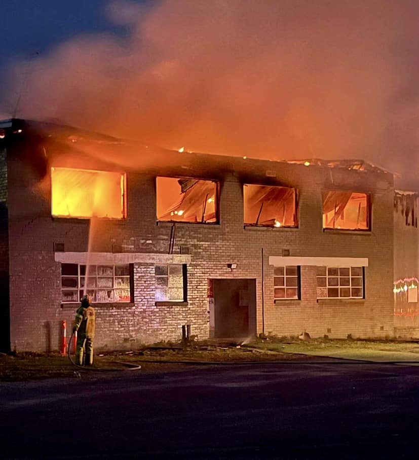 A roof has collapsed and flames can be seen inside a two storey brick building as a lone firefighter sprays water into a window