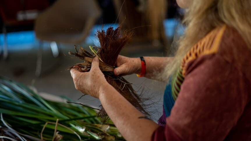 An indigenous woman's hands, weaving a nest from plant materials.