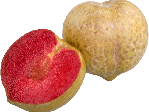 A whole green skinned plum with red blotches sits beside a plum that has been cut in half to reveal its red flesh