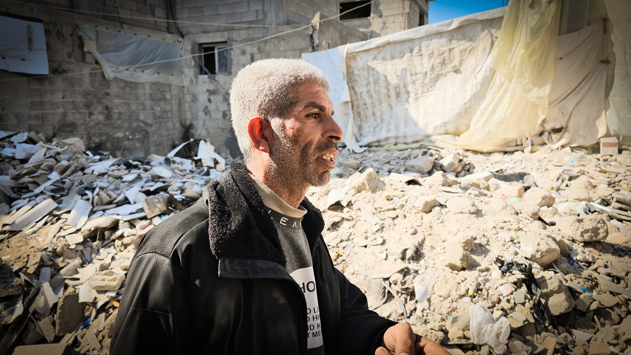 A man wearing a dark jacket searches the rubble of a destroyed building.