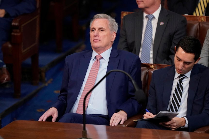 Kevin McCarthy, in a blue suit, leans back looking tense as a staffer hand counts votes for speaker of the House