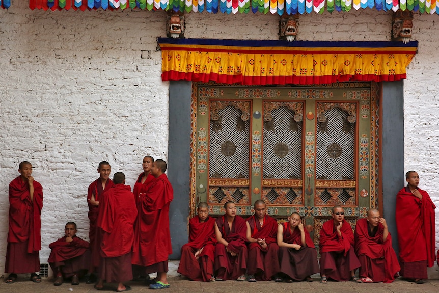 Monks in red robes sit and stand around a temple in Bhutan.