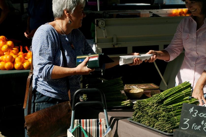 A woman pays for asparagus at a farmer's market.