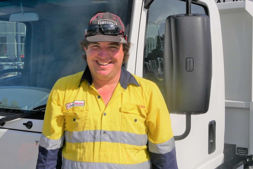 Man with a big smile and wearing hi-vis stands next to a truck
