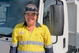 Man with a big smile and wearing hi-vis stands next to a truck
