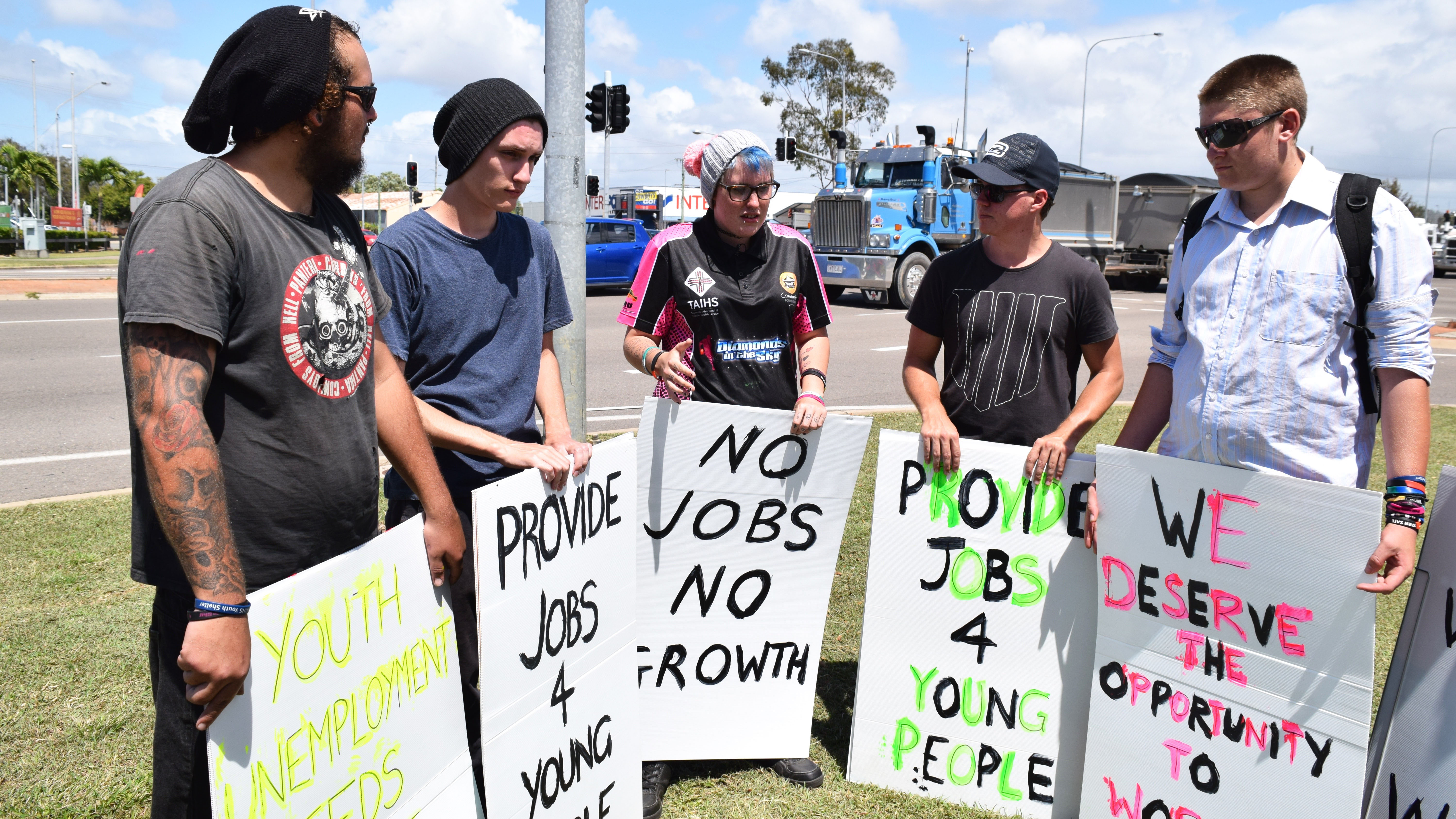 A group of young people stand together holding signs that read "provide jobs for young people".