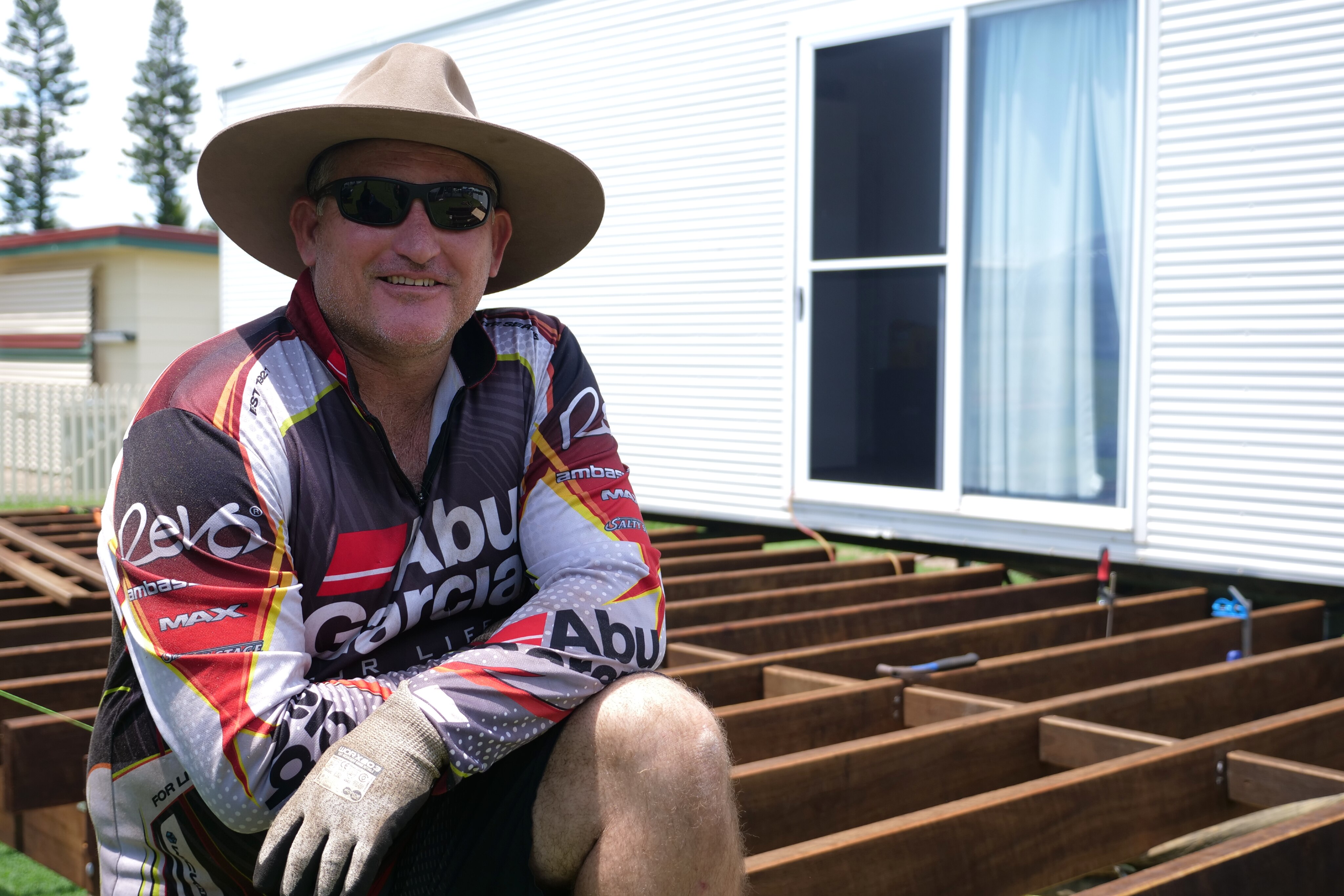 Tyson Sellin sitting on the deck, longsleeve shirt, hat, sunglasses. 