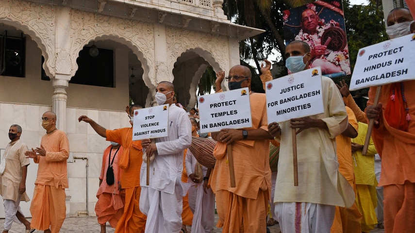 men in orange hindu robes march in temple with signs reading "stop violence against hindus" and "protect hindus in bangladesh"