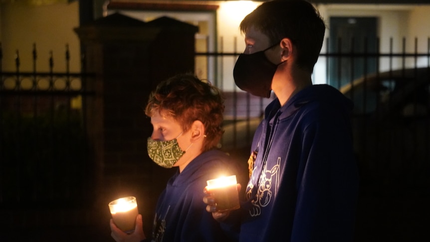 Two boys wearing masks stand in their driveway holding candles.